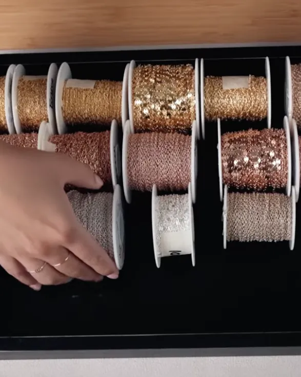 Manos acomodando carretes de cadena dorada y rosada de distintos estilos en una charola de joyería permanente.