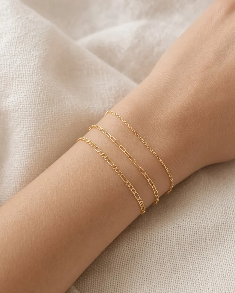 Primer plano de tres pulseras finas de cadena de oro ya soldadas en la muñeca de una mujer.